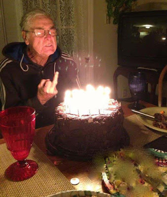 Lustiger alter Mann feiert Geburtstag mit Kuchen und Stinkefinger